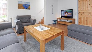 Un salon avec une table basse en bois, des canapés gris, un téléviseur et une porte en bois.