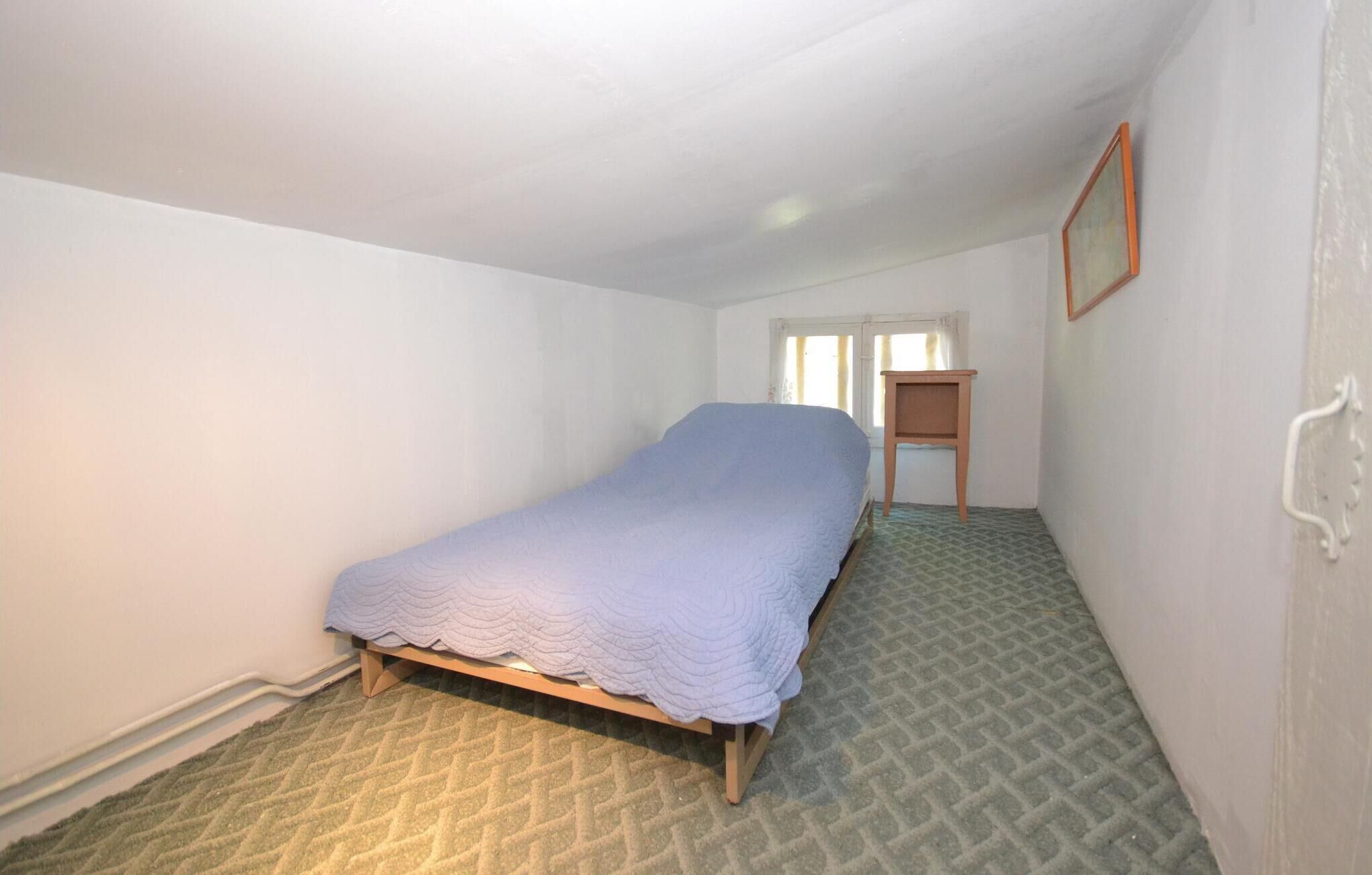 Une petite chambre avec un lit simple, un cadre de lit en bois et un tapis à motifs verts.