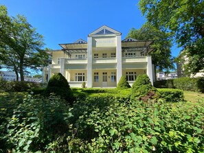 A multi-story building with a central entrance, surrounded by lush greenery and trees.