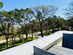A balcony with a view of a coastal landscape, including trees and a clear sky.