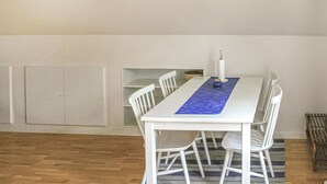 Een eethoek met een witte tafel en stoelen, een blauwe tafelkleed en een witte kaars op de tafel.