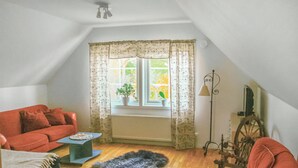 Een gezellig zolderkamer met een rode bank, een klein tafeltje, een potplant bij het raam en een antieke spinning wiel.