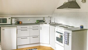 Een kleine keuken met witte kastjes, een magnetron, waterkoker, spoelbak en kookplaat.