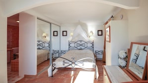 A bedroom with a bed, a mirror, and a bathroom visible through an archway.