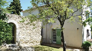 A stone building with a green door, a small garden with a tree, and a stone pathway leading to an arched entrance.