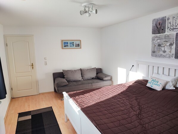 A bedroom with a bed, a sofa, a door, and a ceiling light.