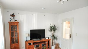 En stue med et tvmøbel i træ, et fladskærms TV, en potteplante og en dør med lysarmatur.