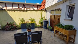En terrasse med et bord og stole, omgivet af krukkeplanter og en træbænk.