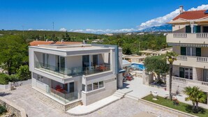 Ein modernes, zweistöckiges Gebäude mit Glasbalkon, Pool und Bergblick.