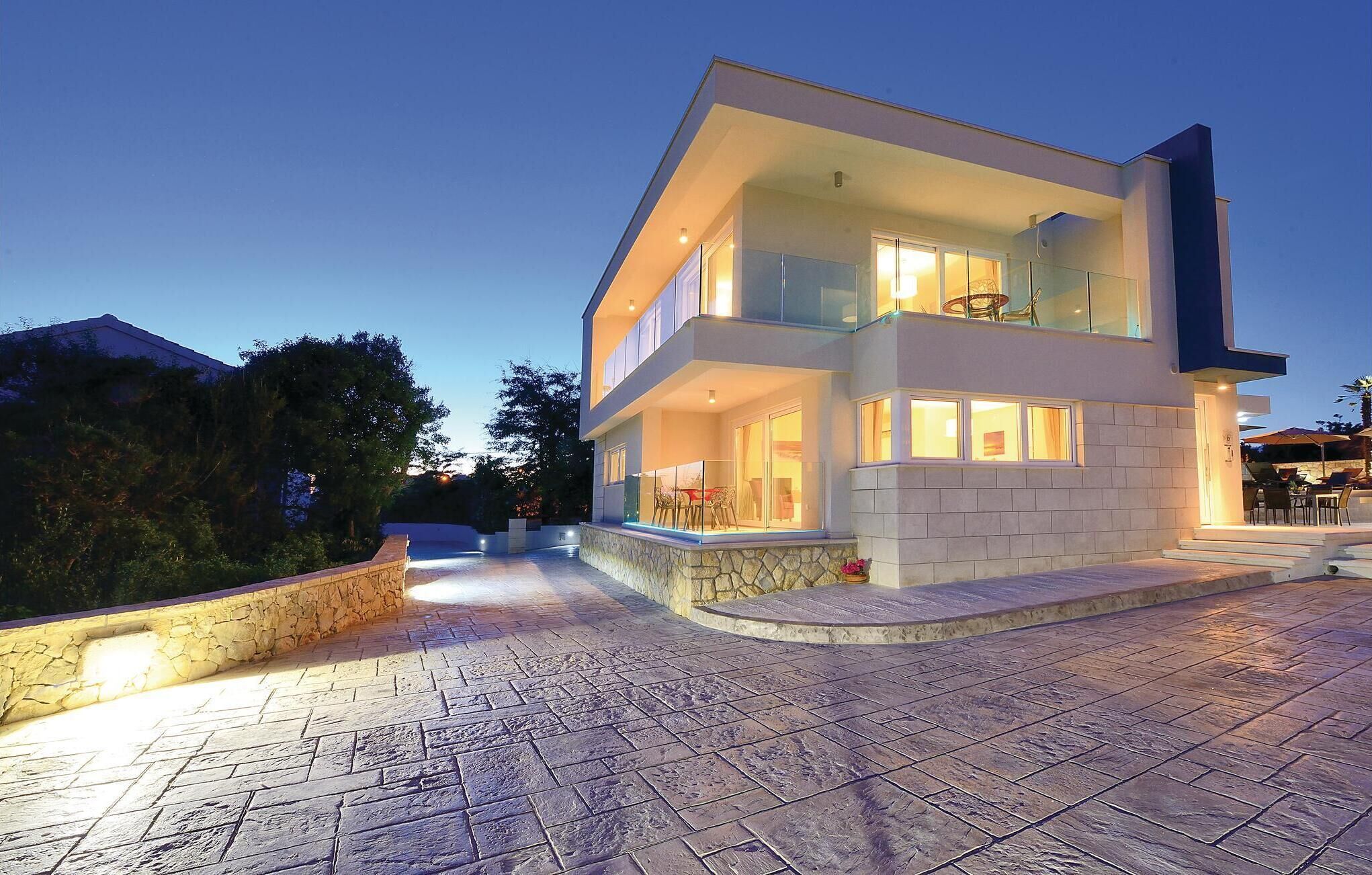 Une maison moderne à deux étages, dotée de fondations en pierre, de grandes fenêtres et d’un balcon avec un espace salon extérieur.