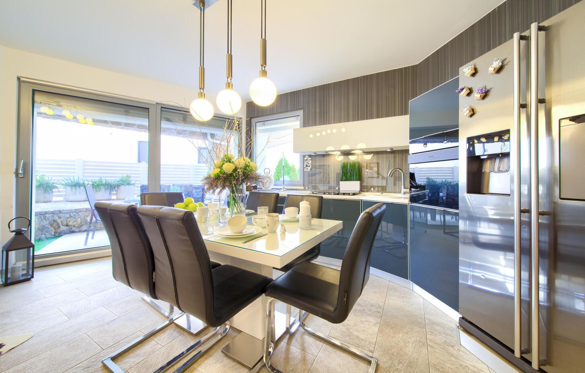 A modern kitchen with a dining area, featuring a stainless steel refrigerator, a glass dining table, and black chairs.