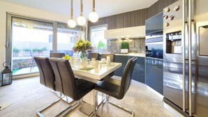 Una cocina moderna con comedor, que incluye un refrigerador de acero inoxidable, una mesa de comedor de vidrio y sillas negras.