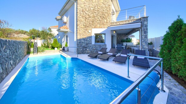 Una villa moderna con piscina, muros de piedra y mobiliario de exterior.