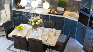 Una cocina moderna con una mesa de comedor preparada para cuatro personas, que incluye un florero con flores, un cuenco de limones y diversos electrodomésticos.