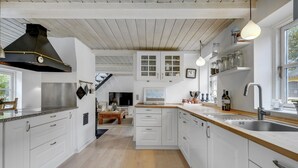 A modern kitchen with white cabinets, a wooden countertop, and a black range hood. There is a dining area with a table and chairs in the background.