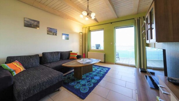 A living room with a sofa, a coffee table, and a television. There are two windows and a door leading outside. - Peeneblick - Reusenhof on the lagoon (Usedom)