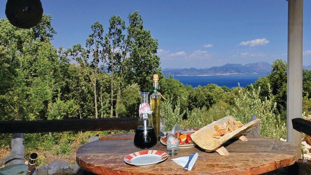 A round wooden table with a plate, a glass, a bottle, and a bowl of bread on a terrace overlooking a scenic view of the sea and mountains. - Awesome home in Crkvice with house sea view (Crkvice)