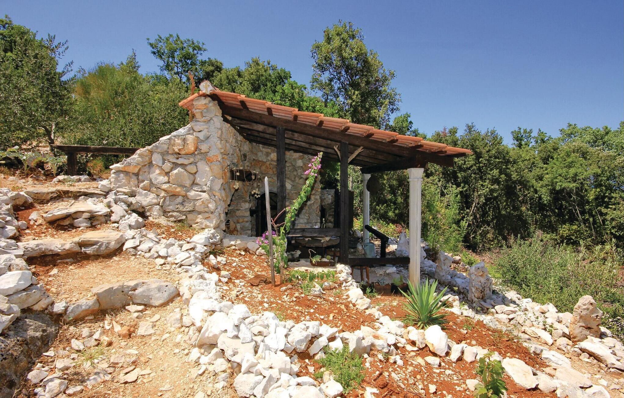 A rustic stone building with a wooden roof, surrounded by rocks and sparse vegetation.