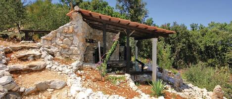 A rustic stone building with a wooden roof, surrounded by rocks and sparse vegetation.