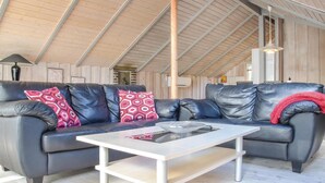 A modern living room with a black leather sofa, a white coffee table, and a wooden ceiling. - Cozy home in Ringkøbing with sauna (Ringkøbing)