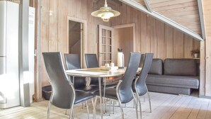 A dining area with a round table, six chairs, a hanging light fixture, a sofa, and a wooden wall. - Cozy home in Ringkøbing with sauna (Ringkøbing)