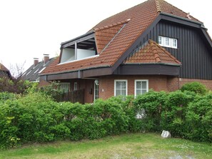 A two-story house with a sloped roof, a balcony on the upper floor, and a brick exterior.