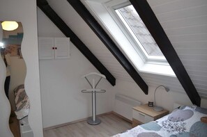 A bedroom with a sloped ceiling, a skylight, a bedside table with a lamp, and a bed with a patterned bedspread.