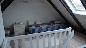 Un petit dormitori d'altell acollidor amb un sostre inclinat, un llit individual amb un estri sol·lit i un taulell de nit amb una làmpada, i una finestra que deixa entrar llum natural.