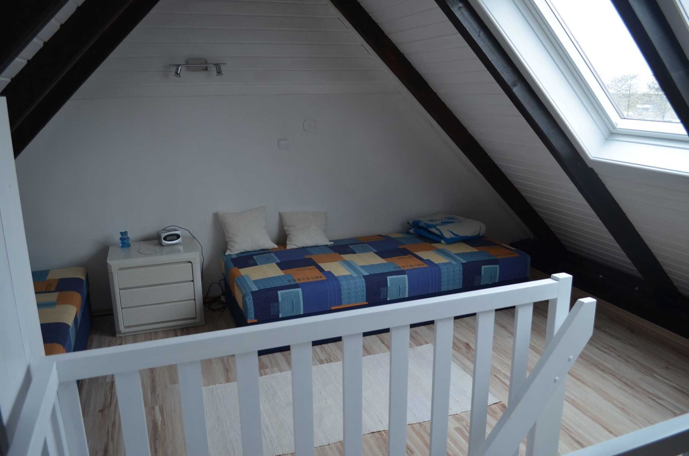 Ett litet, mysigt sovrum på vinden med ett sluttande tak, en säng med ett färgglatt täcke, ett nattduksbord med en lampa och ett fönster som släpper in naturligt ljus.