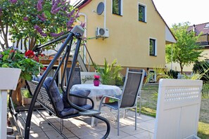 Un patio al aire libre con una silla mecedora, una mesa con una silla y una maceta con flores.