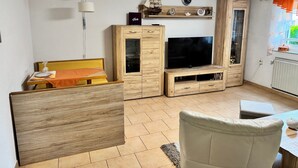 Un espacio habitable compacto con televisor, muebles de madera, una mesa de comedor y un ventanal con cortinas.