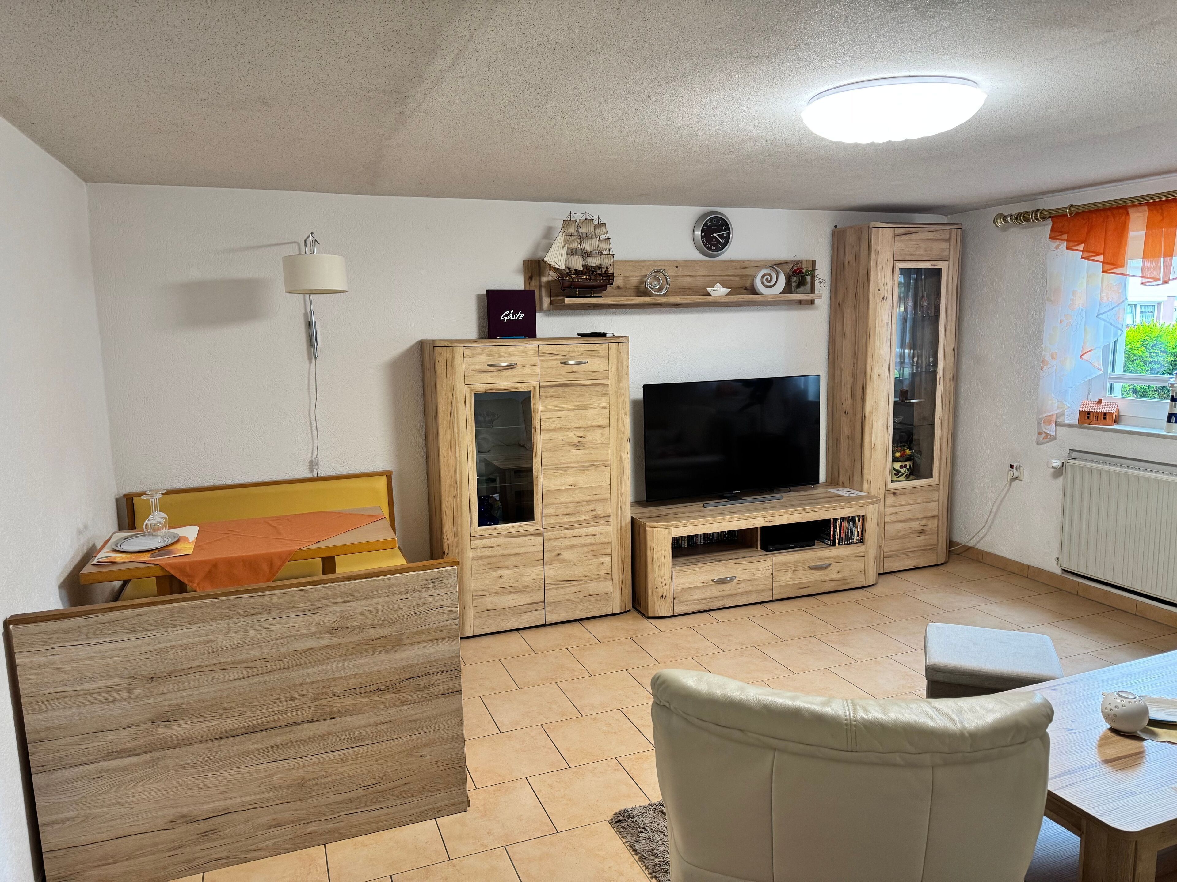 A compact living space with a TV, wooden cabinets, a small dining table, and a window with curtains.