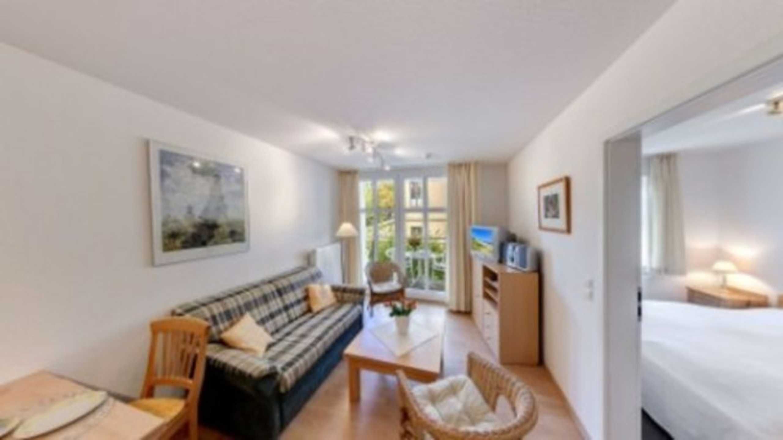 A room with a sofa, a chair, a small table, a bed, and a TV.