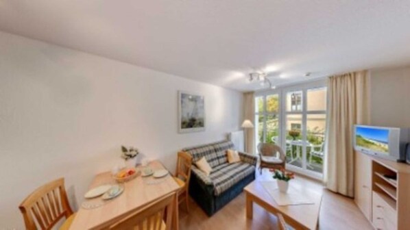 Un salon confortable avec un canapé, une table à manger et des chaises, un téléviseur et une fenêtre avec des rideaux.
