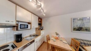 Een compacte keuken met een magnetron, koffiezetapparaat en een eethoek met een tafel en stoelen.