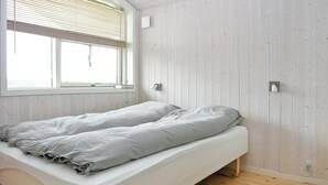 Un letto singolo con materasso bianco e biancheria grigia in una stanza con pareti in legno e una finestra con persiane.