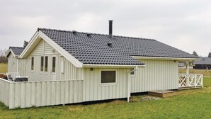 Un piccolo edificio a un piano con tetto spiovente e camino, immerso nel verde e dotato di un patio in legno.
