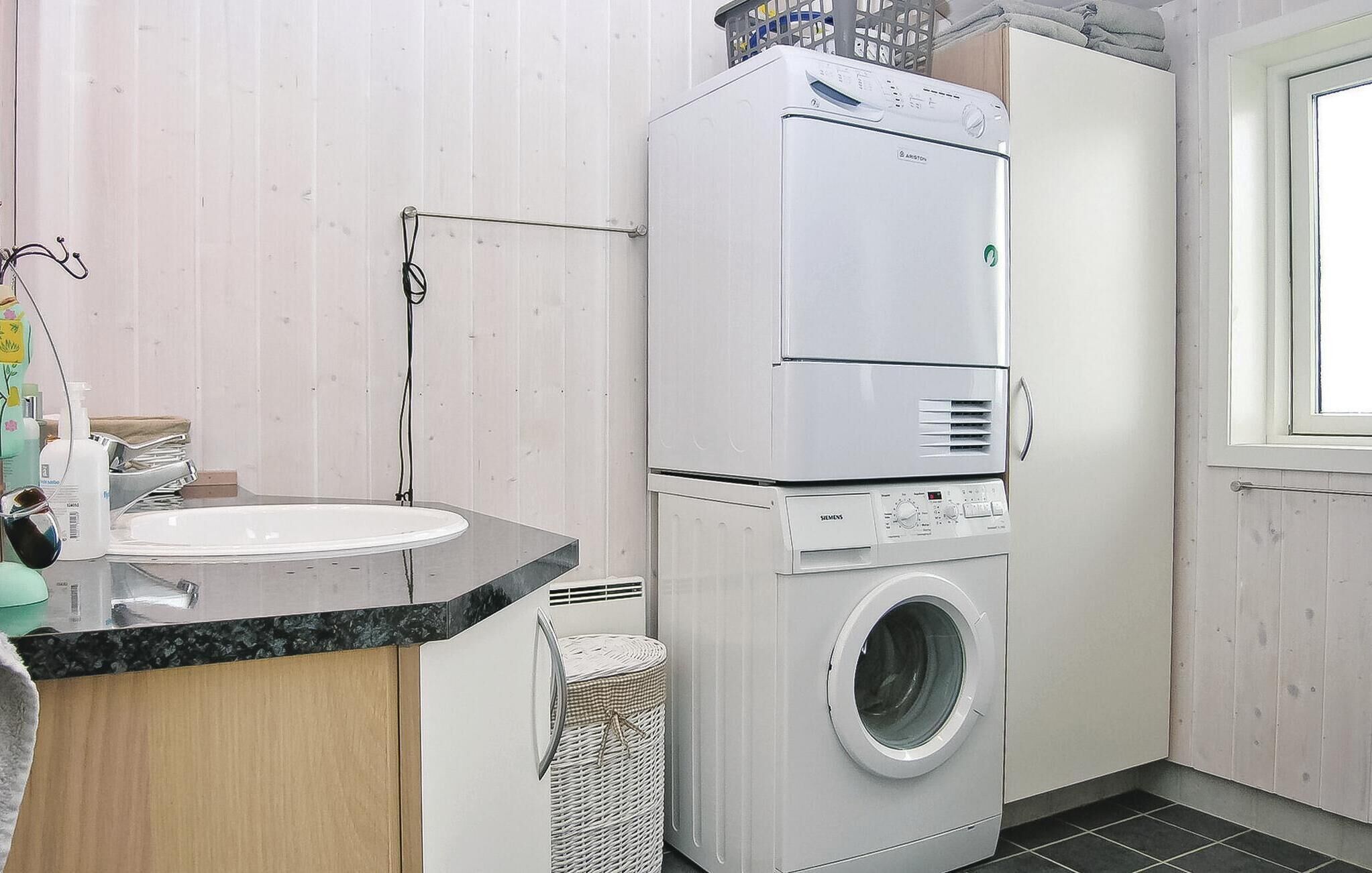A compact laundry room with a washing machine and dryer stacked on top of each other, a sink, and a wicker basket.
