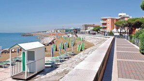 Ein Strand mit einer Reihe von Liegestühlen und einem kleinen Gebäude, vermutlich einer Rettungswache, in Wassennähe.