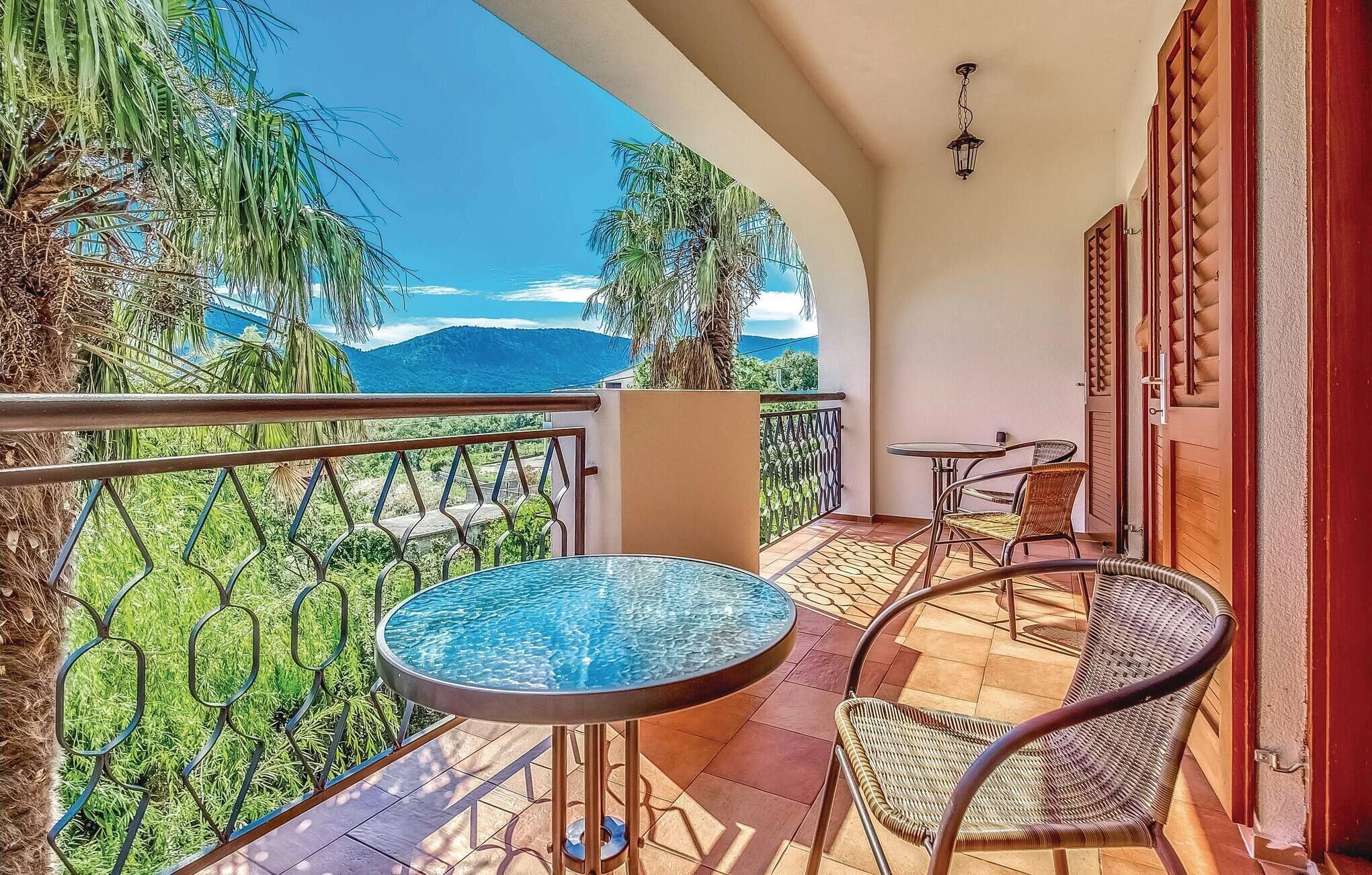 A balcony with a glass table and wicker chairs, overlooking a mountainous landscape.