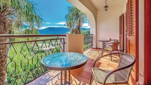 Ein Balkon mit Glastisch und Korbstühlen mit Blick auf eine gebirgige Landschaft.