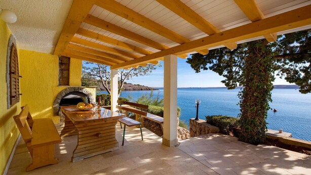 A covered outdoor seating area with a stone fireplace, wooden furniture, and a view of the sea. - 1 bedroom beach front apartment in Lukovo Sugarje (Lukovo Sugarje)