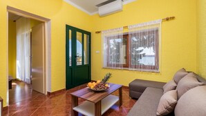 A living room with a sofa, a coffee table with fruit, a green door, and a window with curtains. - 1 bedroom beach front apartment in Lukovo Sugarje (Lukovo Sugarje)