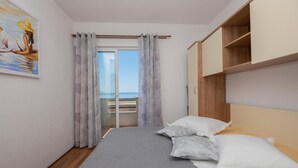 Une chambre avec un lit, une vue sur la mer par une porte coulissante et un tableau au mur.