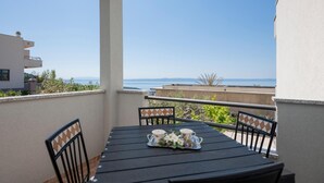 Un balcon avec une table dressée pour deux personnes, donnant sur une étendue d’eau et sur des collines lointaines.