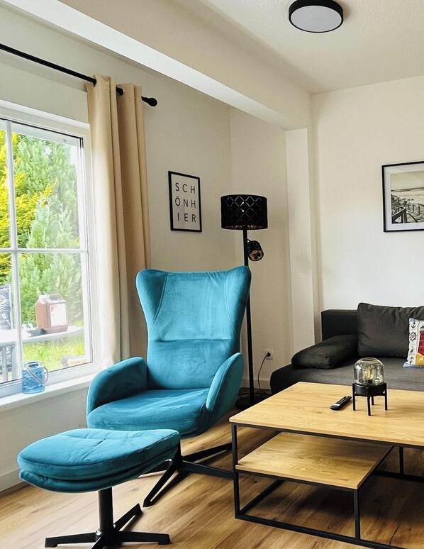 Una sala de estar moderna con un sillón azul turquesa, una mesa de centro de madera, una lámpara de pie negra y un sofá negro.