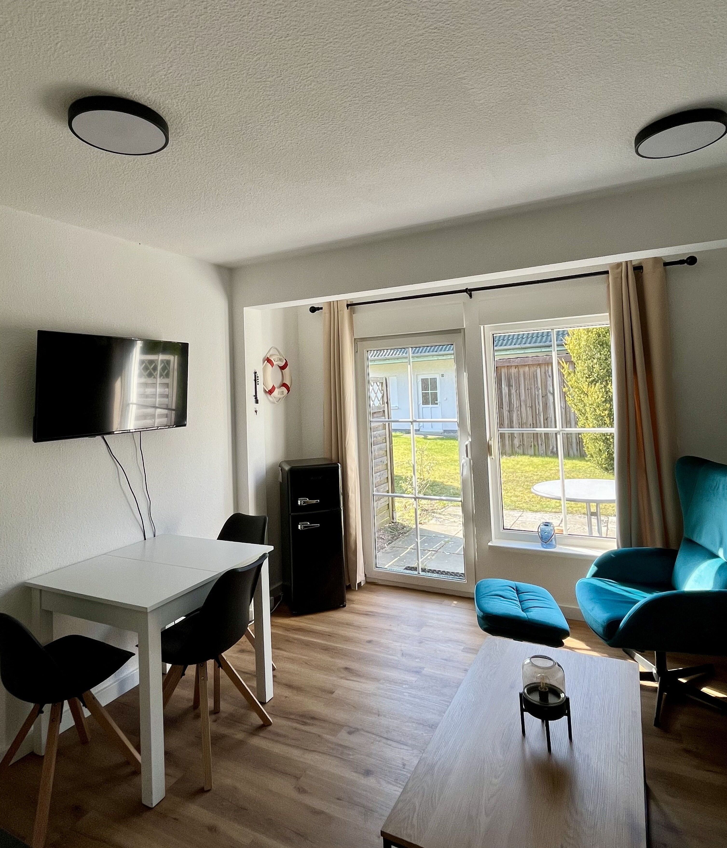 Een moderne woonkamer met een flatscreentelevisie, een eettafel met stoelen, een blauwe bank en een groot raam met gordijnen.