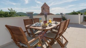 A wooden table set with plates, cups, and a pitcher on a terrace with a view of a brick structure and hills. - Beautiful home in Blizina Gornja (Blizina Gornja)