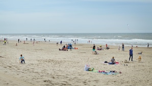 Een strand met mensen, zandkastelen en een vlieger in de lucht.