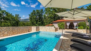 Ein Schwimmbecken mit Steinmauer, Liegestühlen und einer überdachten Terrasse.